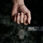 a man is holding an old hamsa amulet, also known of the hand of fatima or the hand of mary, on a black mottled background